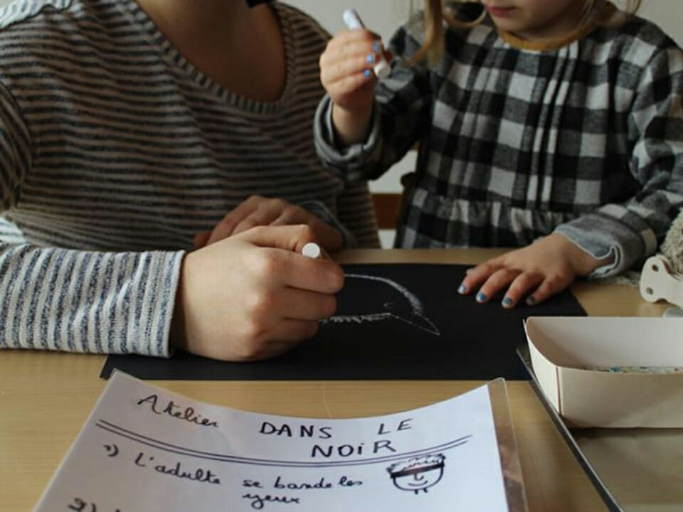 Une adulte et une enfant dessinent au crayon blanc sur une feuille noire