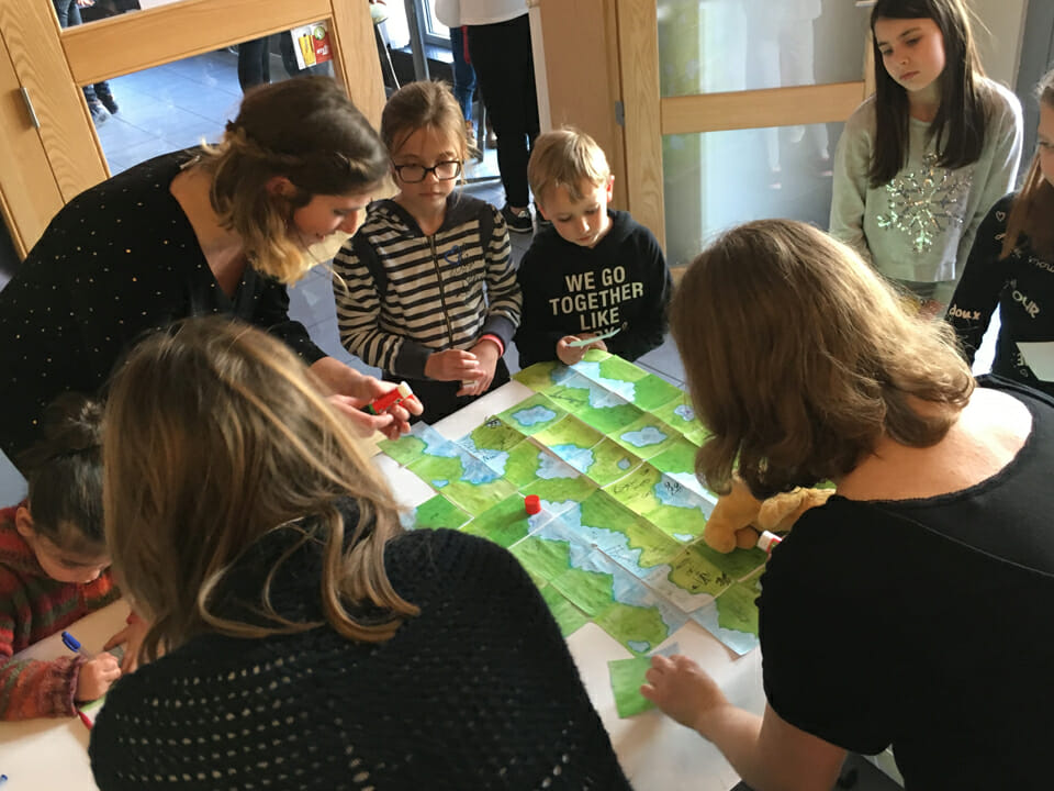 Plusieurs enfants autour d'une table travaille sur une grande carte imaginaire verte.