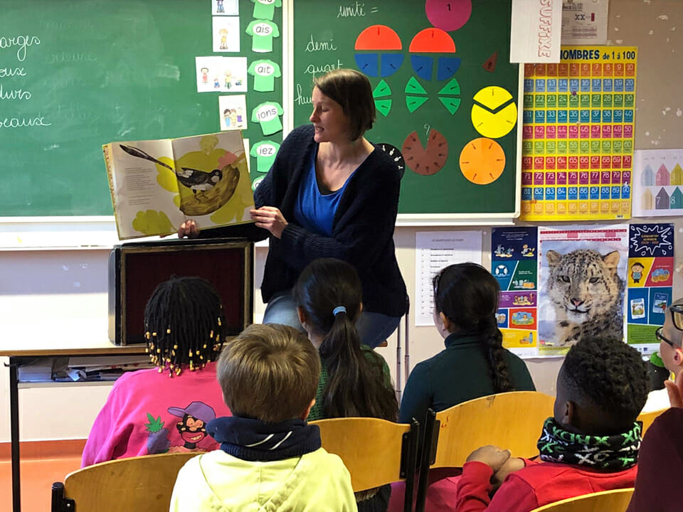 Une animatrice tient un livre sur son côté droit et le lit à une classe d'enfants de primaire.